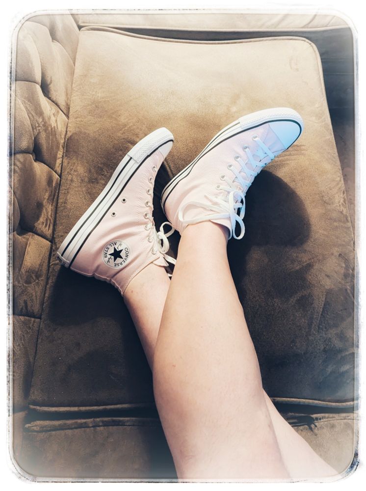 Converse Hightop-Sneaker in zartem Rosa, an semi-trainierten Waden auf einem braunen Sofa.