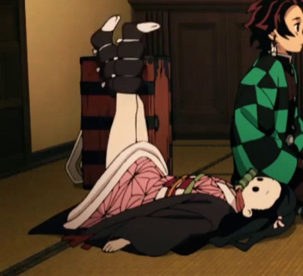 a man in a green and black checkered shirt sits next to a girl laying on the floor