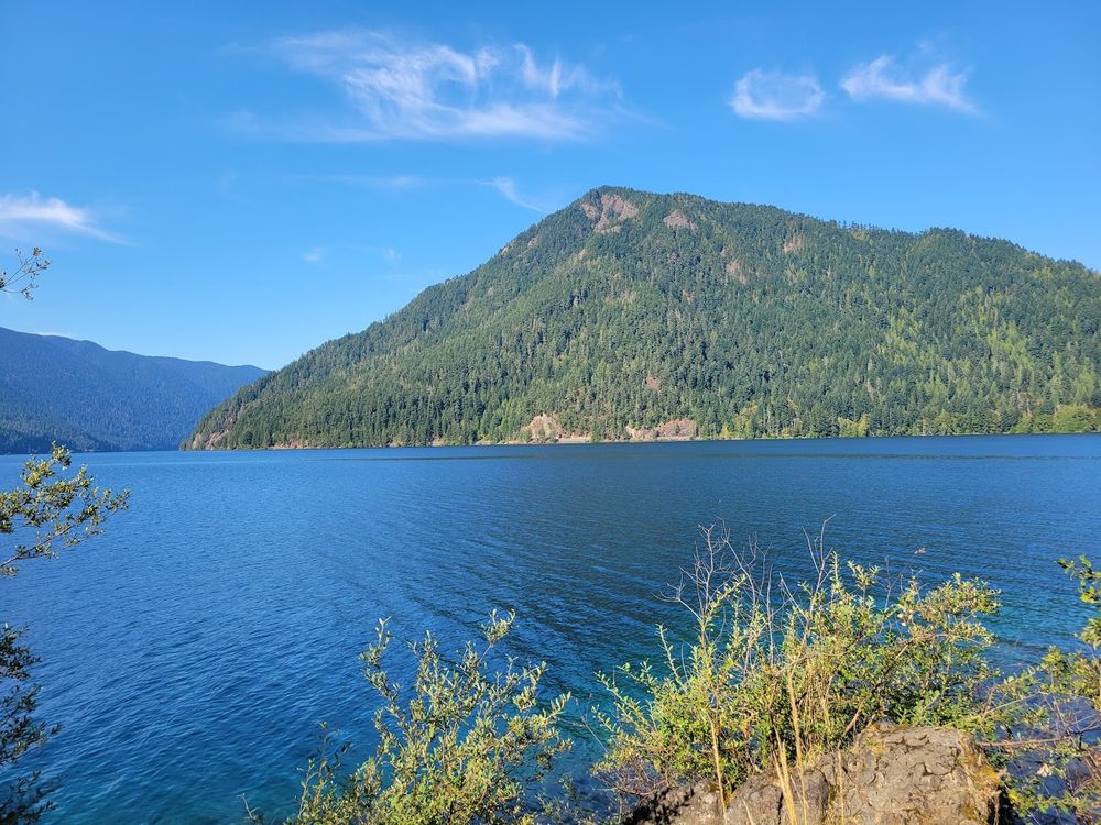 a mountain rising out of a blue lake. the sky is bright blue and there are wispy white clouds. 