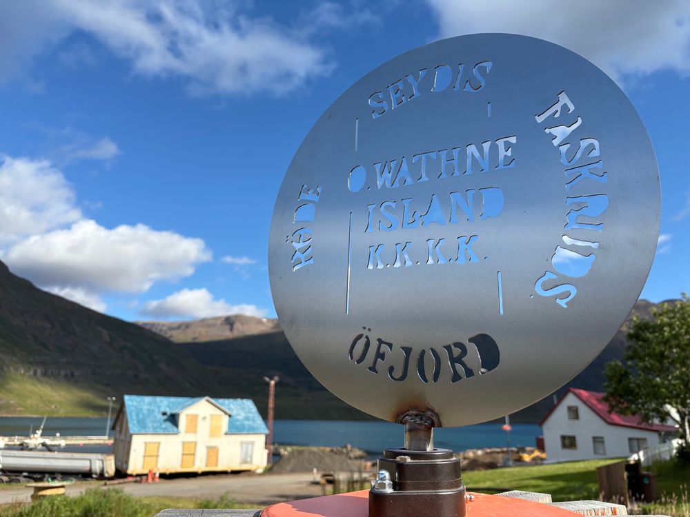 Closeup of a round sign with Seydisfjord in the background 