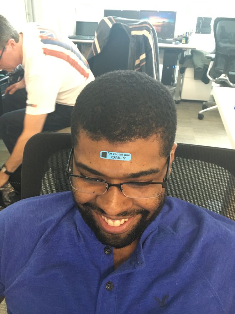 A man smiles with a “for rectal use only” sticker on his forehead.