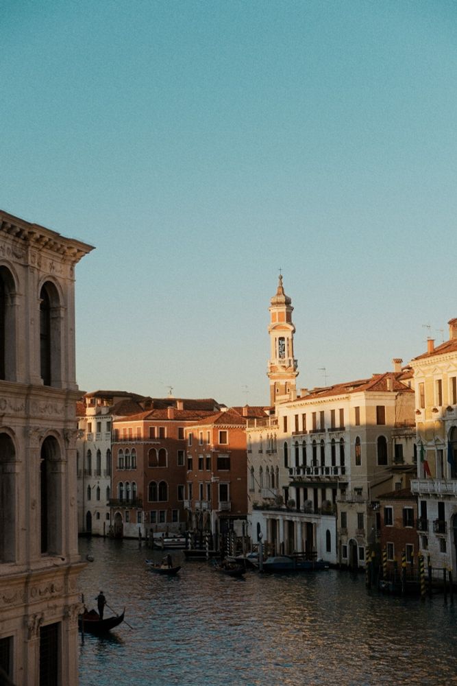 Venice at sunset. A thin strip of golden light illuminates the tops of the buildings as a lone gondola moves through the darker water below.