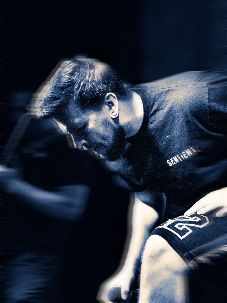 Lead singer of the heavy metal Sentient (band) leaning over and resting before screaming into a microphone. The colour tones are mono, with a blue shade for the shadows and midtones.