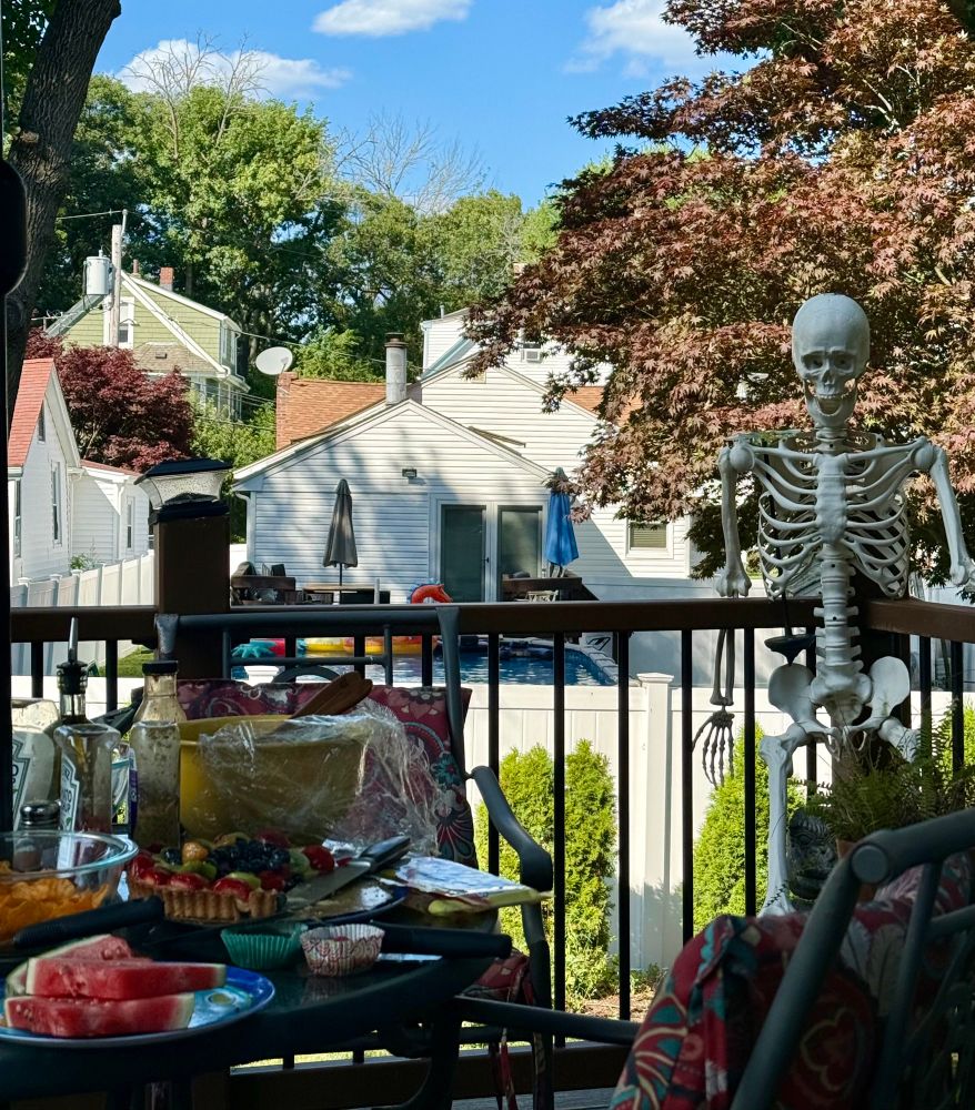 a life-size skeleton looms over a backyard barbecue snack spread 