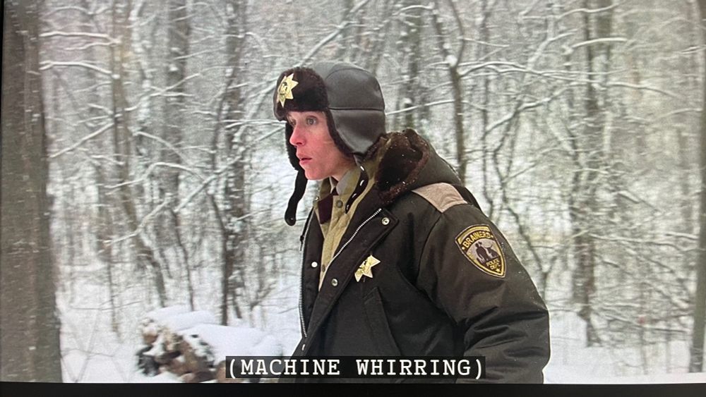 Screen capture of the film "Fargo" with Francis McDormand walking in snow with subtitle [Machine Whirring]
