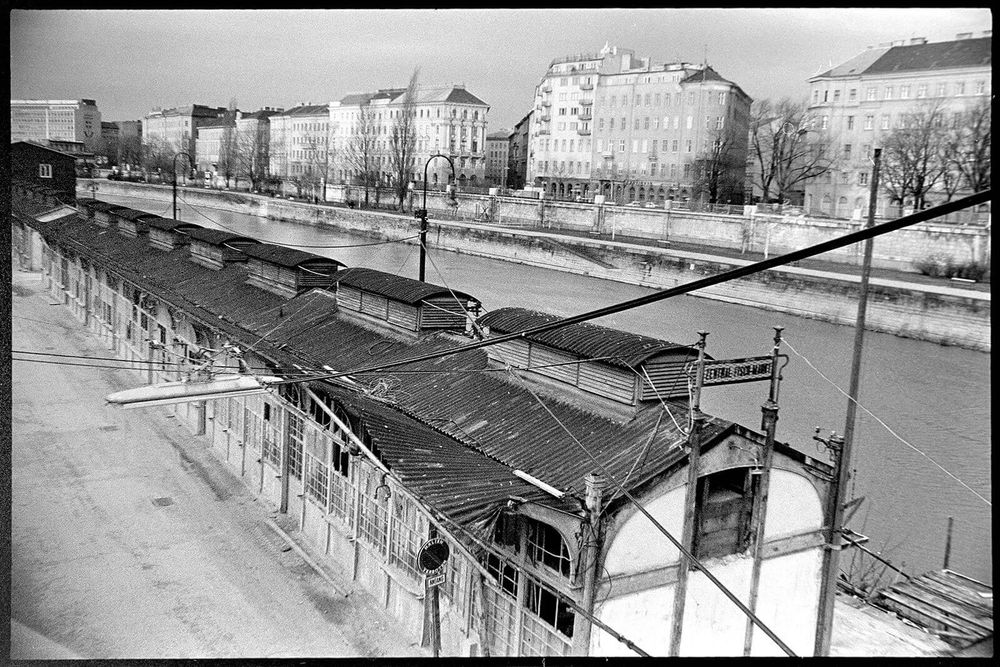 SW Foto. Der Donaukanal zieht sich quer durchs bild , im Hintergrund die Häuserzeile stadtauswärts, im Vordergrund die einstöckige Reihe der Zentralfischmarkt-Stände.