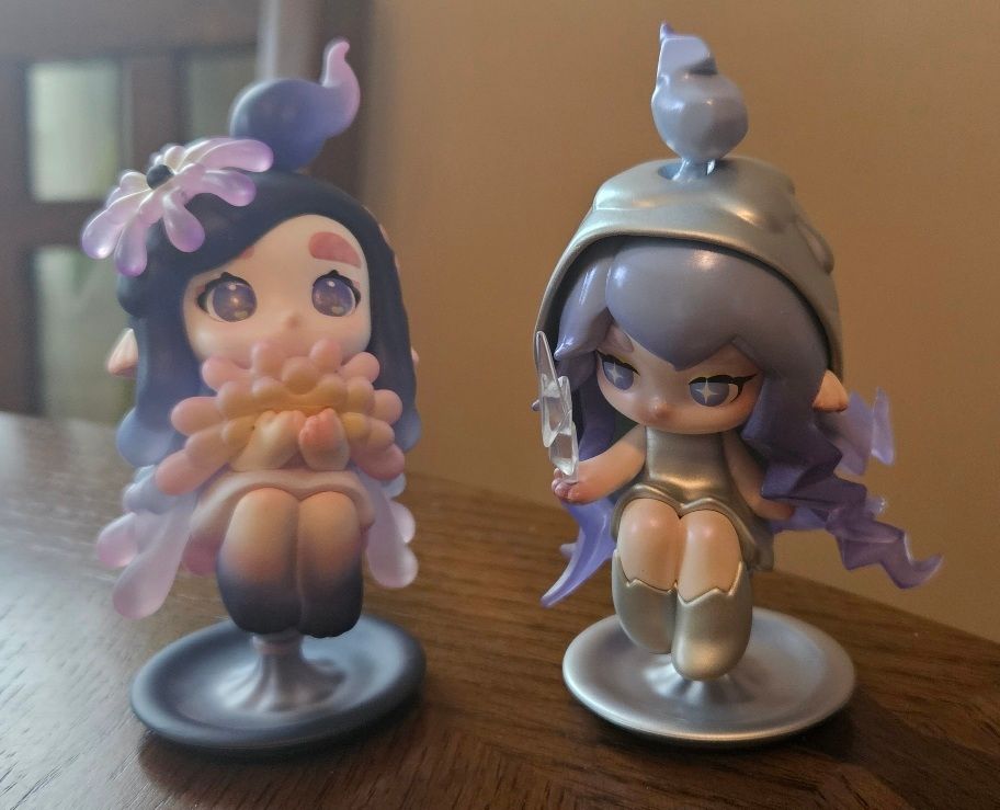 A photograph of two vinyl figures of chibi girls resembling candles, themed on fireworks (left) and lightning (right).