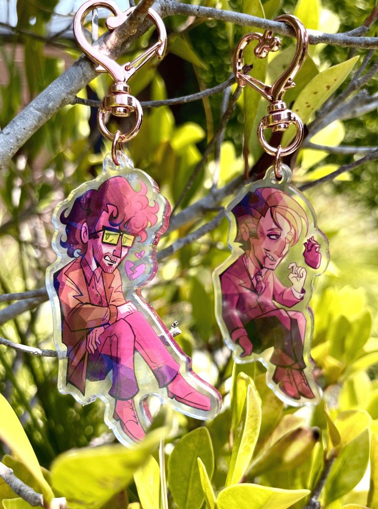 Acrylic Keychain Charms of Will Graham and Hannibal Lecter. Will has green-tinted glasses and a green coat over a red flannel, looking apprehensive with a broken heart - While Hannibal wears a red suit and has blood dripping from his mouth, his heart more realistic and anatomically correct.