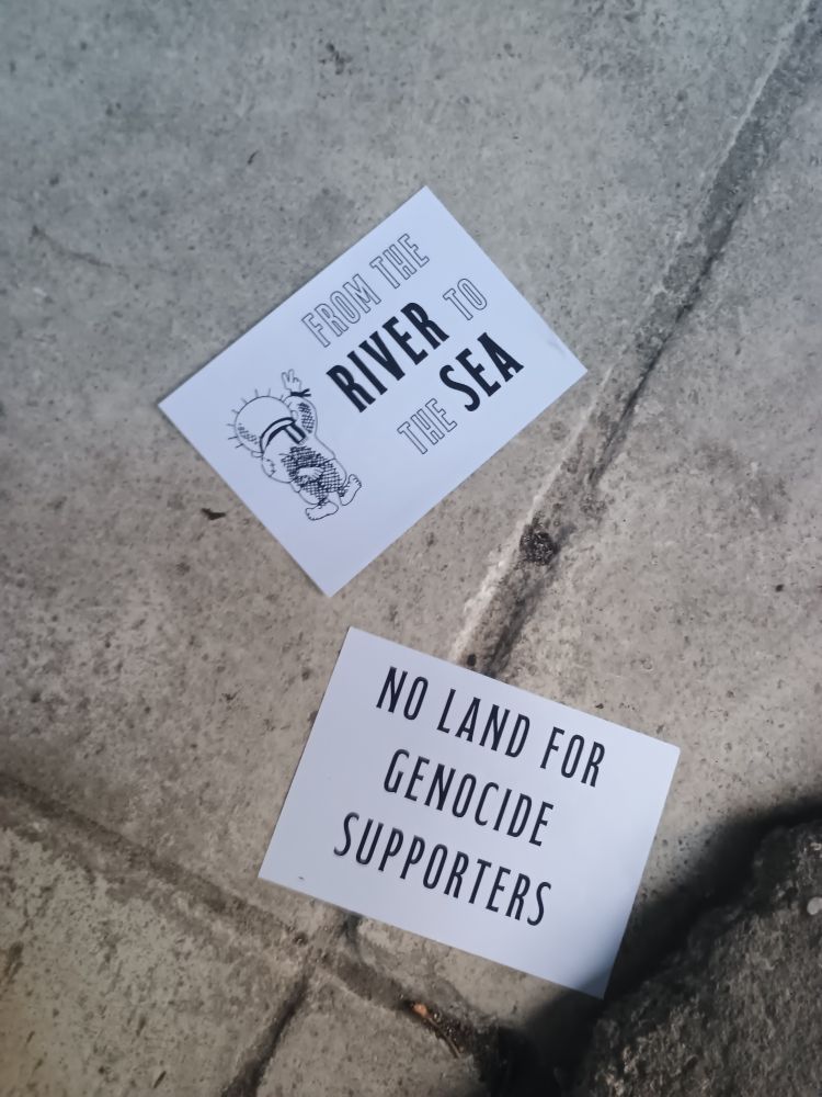 The image shows two leaflets placed on a sidewalk. The leaflet on the top reads "From the river to the sea" and features an illustration of a person wearing a traditional keffiyeh. The leaflet on the bottom reads "No land for genocide supporters."