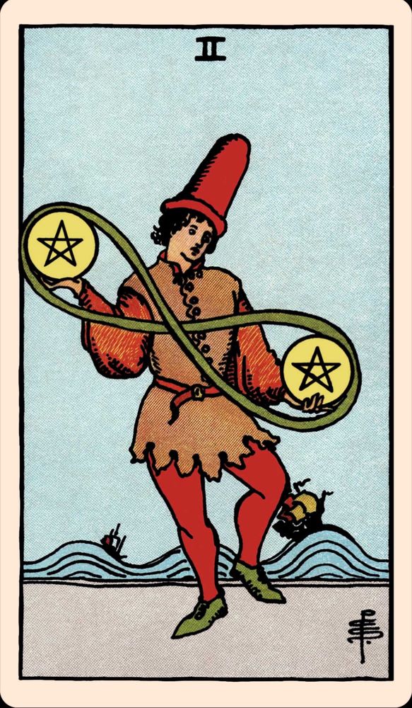 A tarot card: Two of Pentacles. A young man dressed in an orange costume of a entertainer dances while juggling two pentacles in his hands. The two pentacles he holds are joined by a cord making a figure 8 on its side. Behind him two ships are braving a rough sea and are being tossed about in the waves.