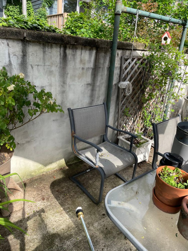 Patio table and chair with a dirty concrete wall behind. The wall has dark streaks starting at the top. The patio floor is also dirty