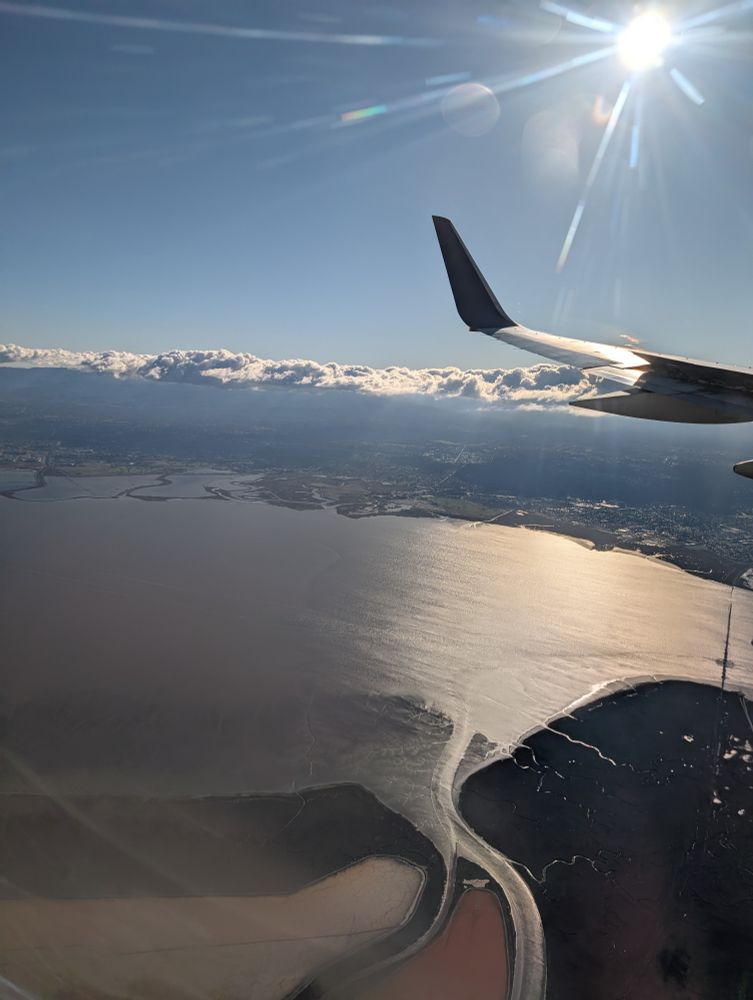A view of the bay flying into SF. The sun is shining. The water glitters. Clouds hover delicately over the horizon.