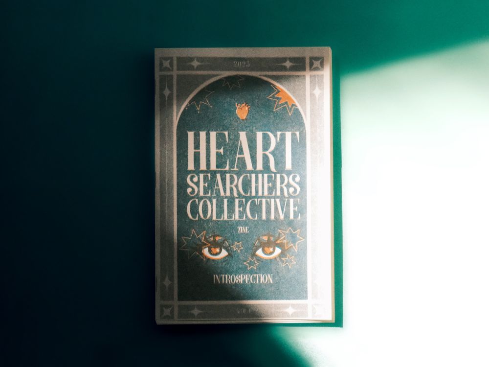The cover of The Heart Searchers Collective Zine. It is Volume one, the theme is introspection and it was printed in 2025. The design is art deco inspired with two sparkling eyes, and is riso printed in teal and orange.