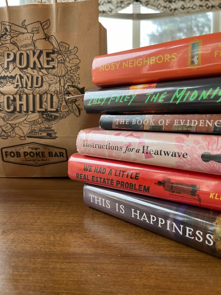 A bag that says, poké and chill related to sushi meal, alongside a stack of books with the titles: nosy, neighbors, the midnight feast, the book of evidence, instructions for a heat wave, we had a little real estate problem, and this is happiness.
