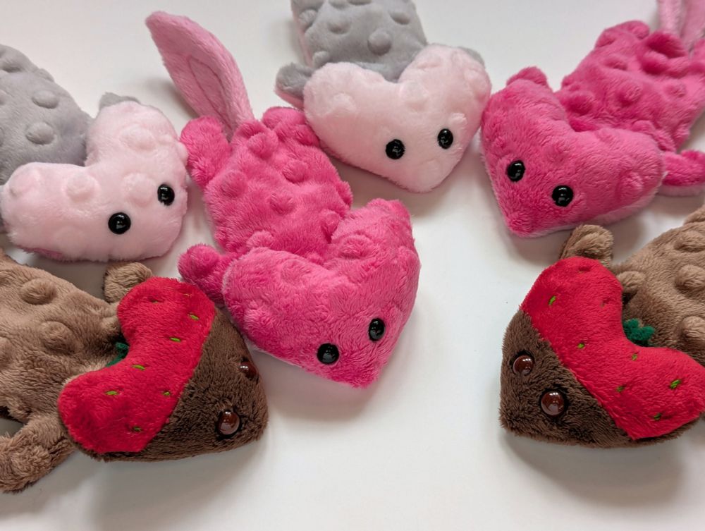 Six palm-sized beanie diplocaulus plushies, newt-like critters with wide heart shaped heads and beady eyes. They're made with dimple textured minky in 3 different designs.
