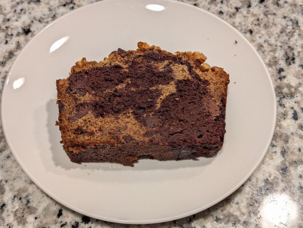 Slice of a loaf of chocolate banana bread topped with walnuts.