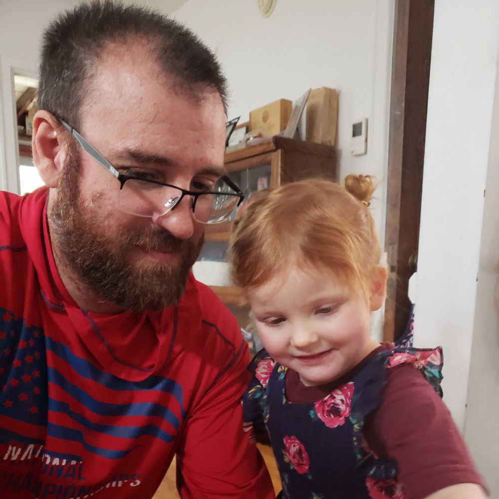 A man and little red headed girl, with space buns, look at a shopping list off screen.