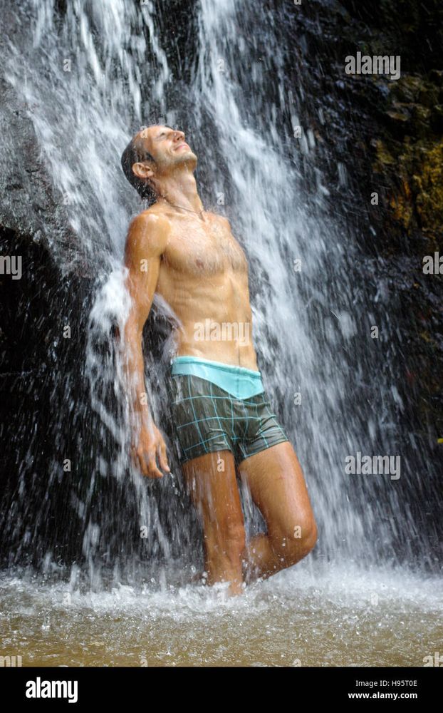 relaxed man bathing under a waterfall