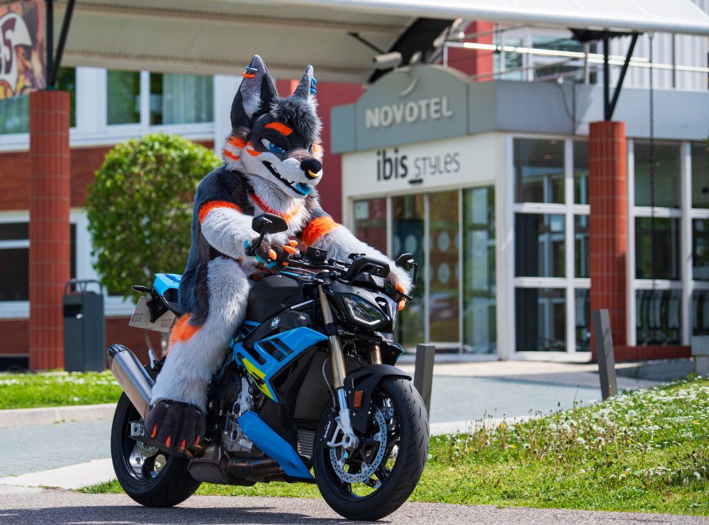 Ethyos in fursuit riding a motorcycle in front of Fauntastic hotel