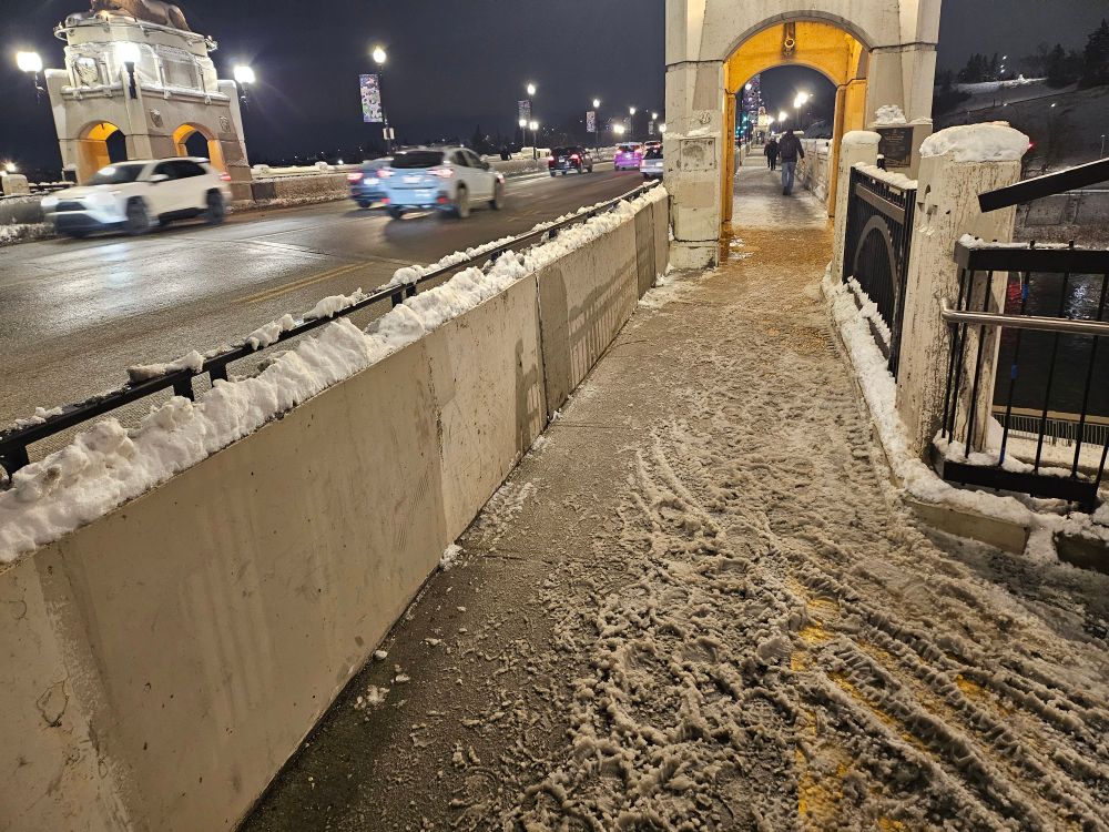 Bare road and traffic and a pathway choked with snow and slush 