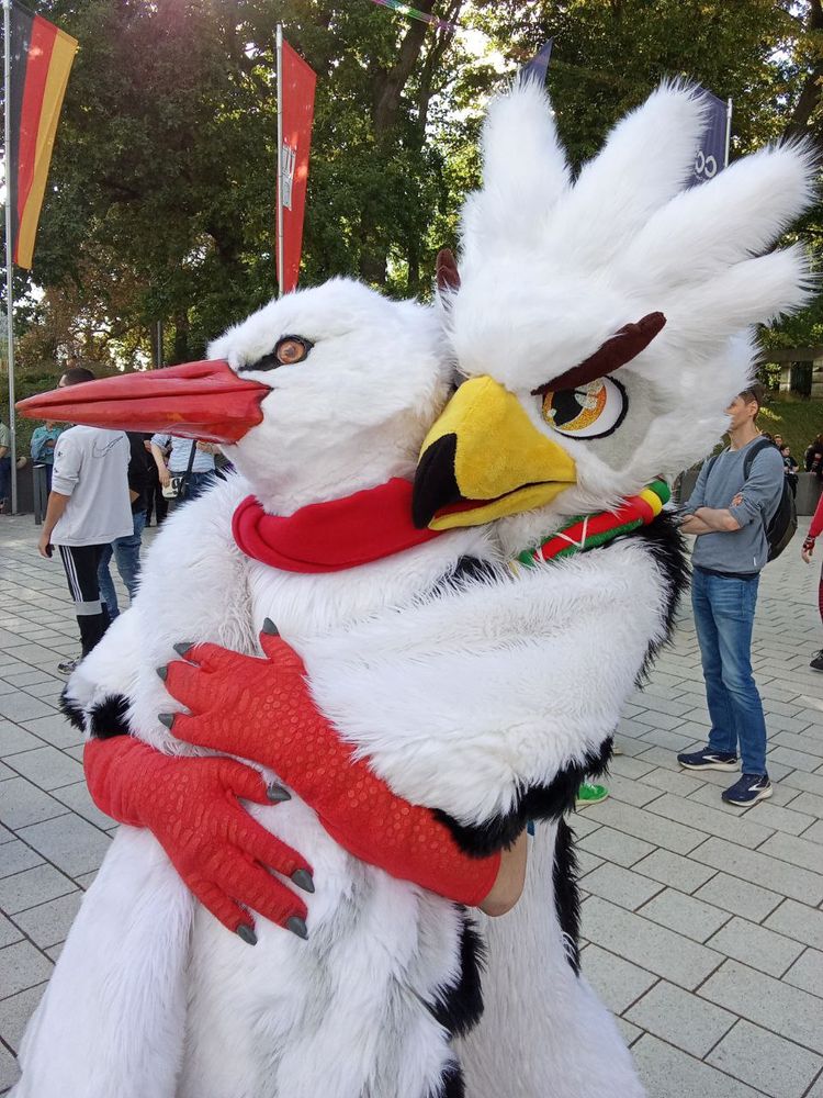 a Teba cosplayer hugging a stork fursuiter from behind