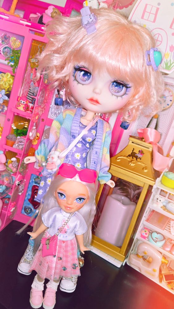 Big-headed Blythe doll with her Rainbow High doll little sister. They're standing together in a lineup