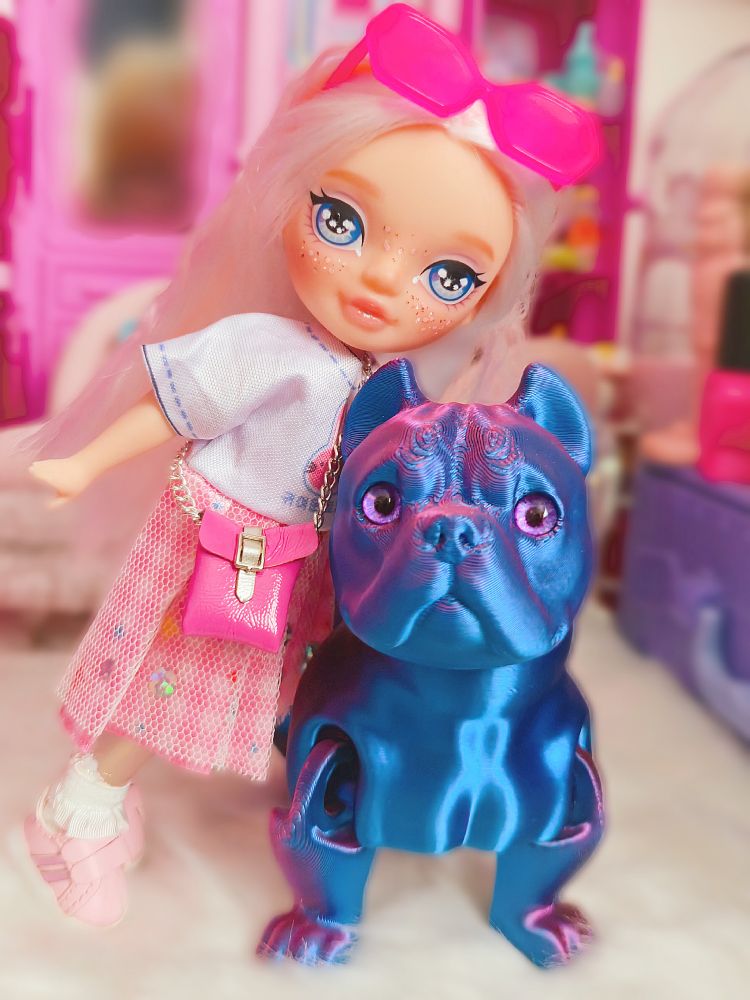 Small white-haired child doll with big shiny blue eyes wearing a pink outfit and pink. She's posing with her blue bulldog for a photo