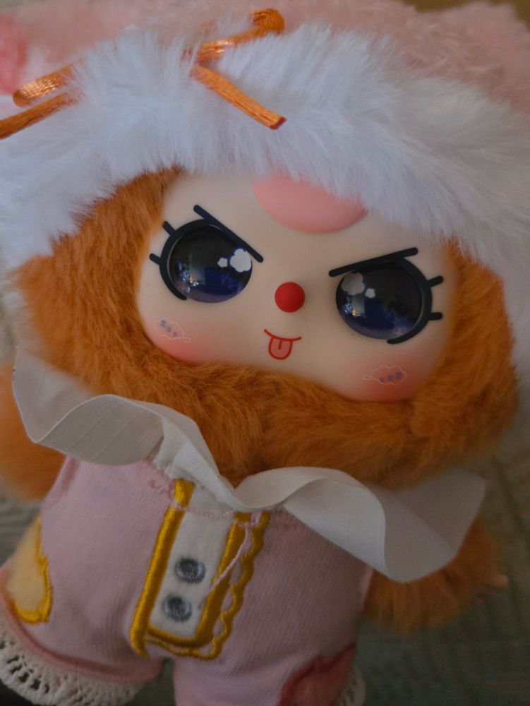 An orange-y brown rabbit with pink hair in a pink and white ruffled outfit, sticking out his tongue and making a mischievous little face