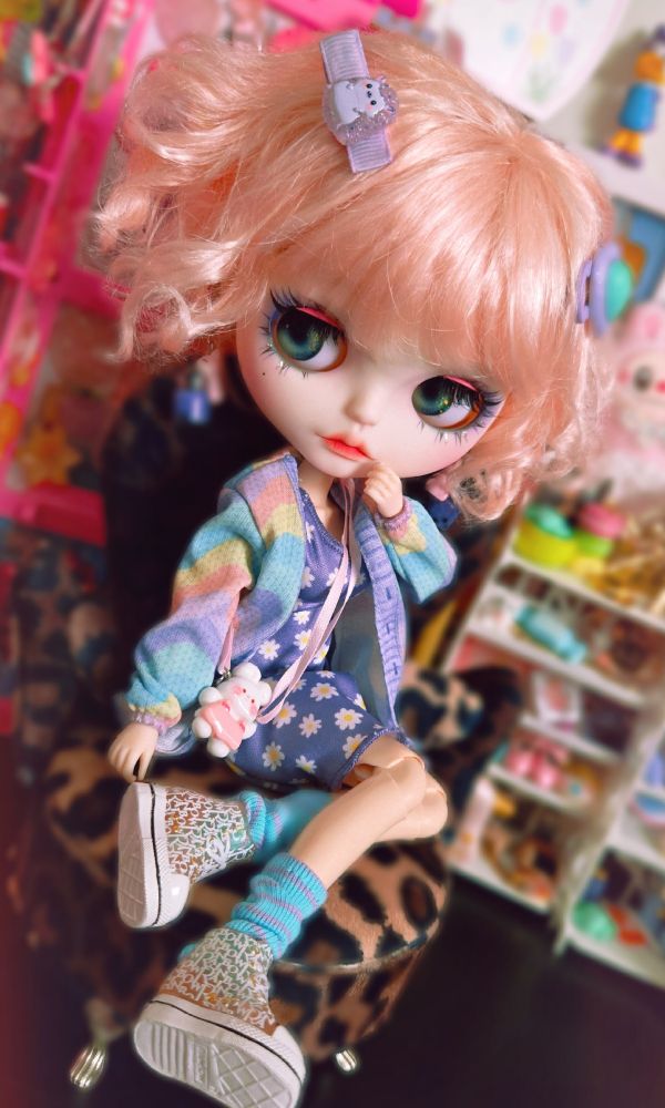 The doll looking curiously to the left with her hand up by her face