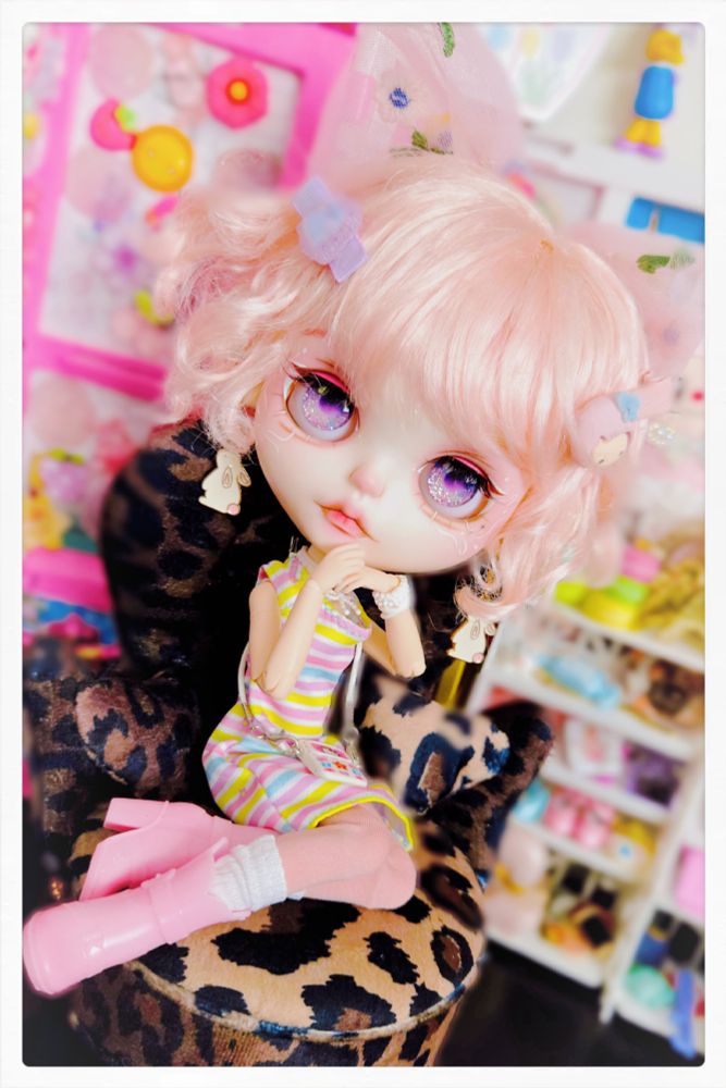 The doll seated in the chair with her chin leaning on her hands and looking at the camera with sparkling purple eyes