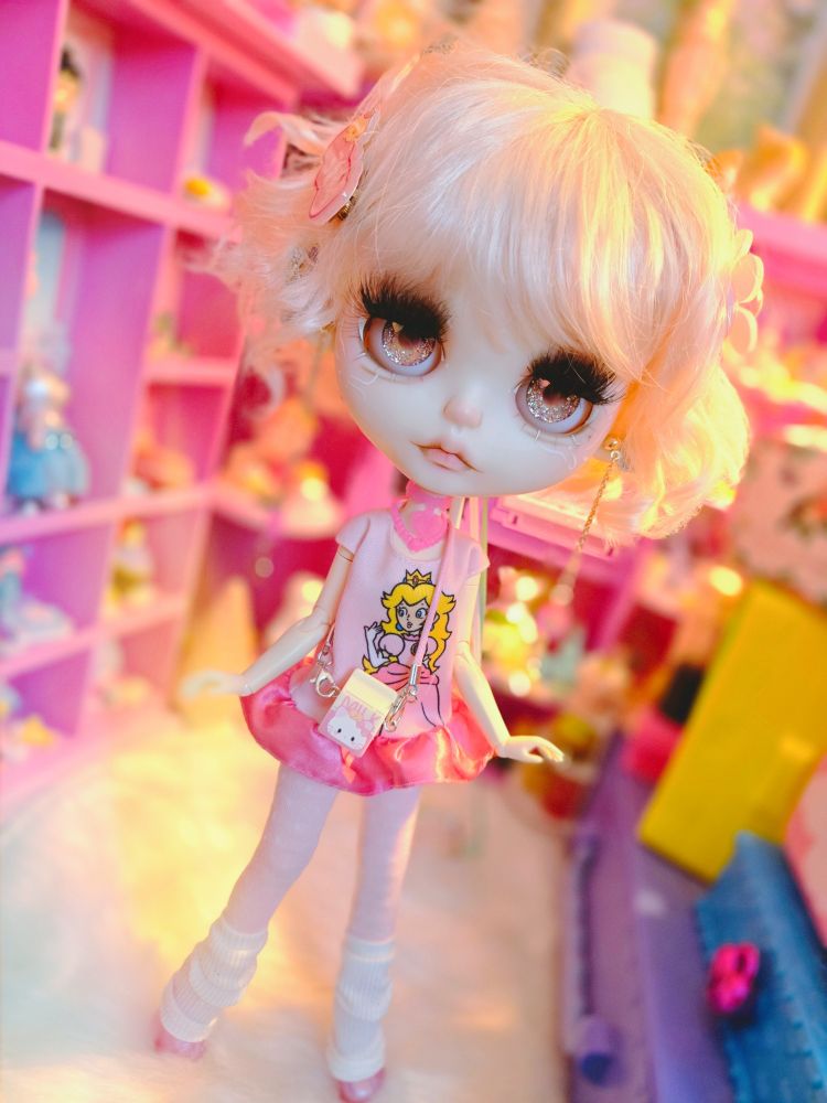 Big-headed Blythe doll with golden brown eyes and a pale pink curly bob. She's wearing a pink ballet-style outfit and posed gracefully in a bright pink dressing room