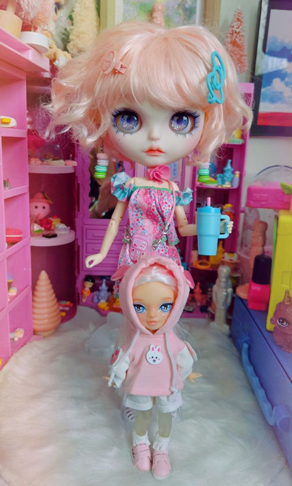 Big-headed Blythe doll with pink hair and a short white-haired little sister doll standing together in a line