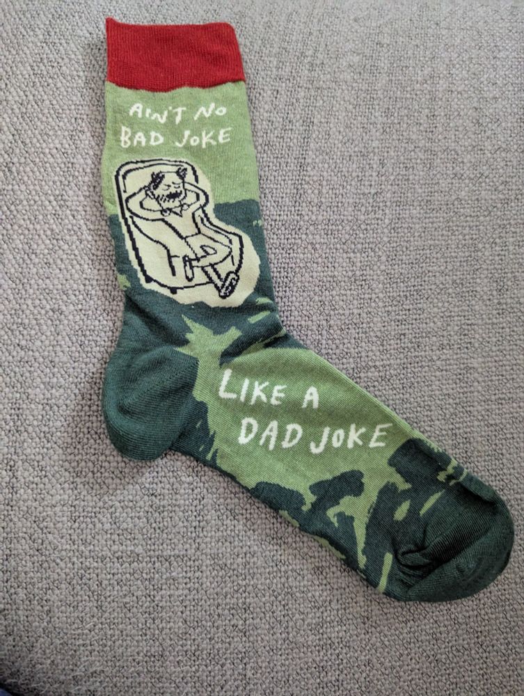 Green and red sock with a picture of a man on a recliner.  Surrounding area the words "ain't no bad joke like a Dad joke."
