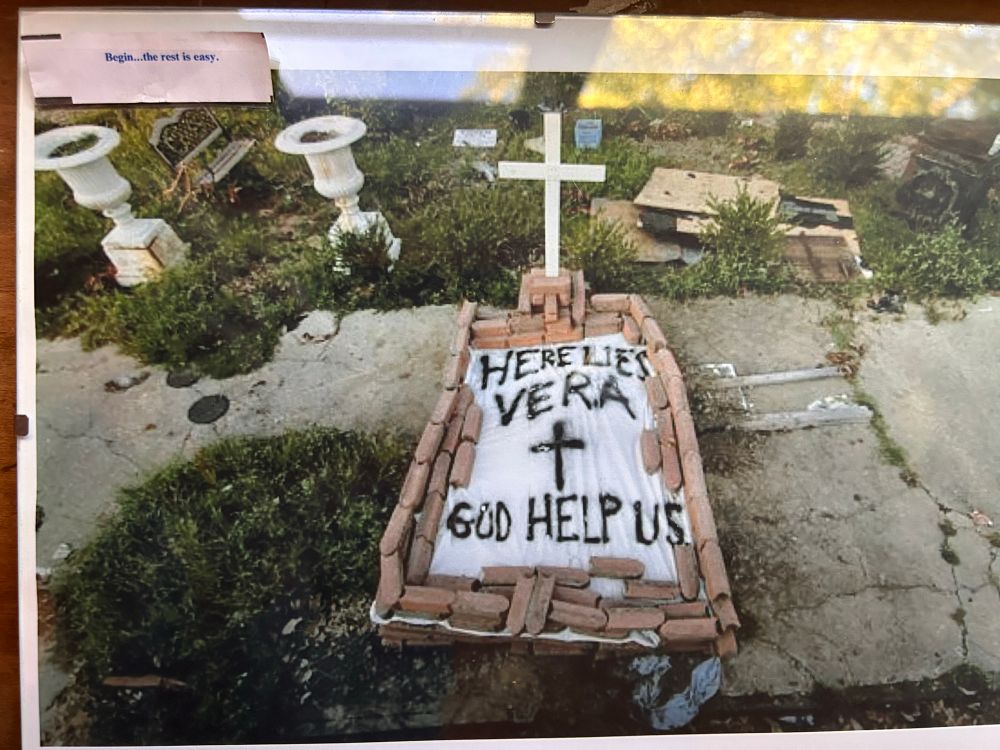 NY Times photo of the handmade grave of a Hurricane Katrina victim. A sheet with the words “Here Lies Vera, God Help Us” covering a body; terracotta tiles as weights to keep the sheet in place.