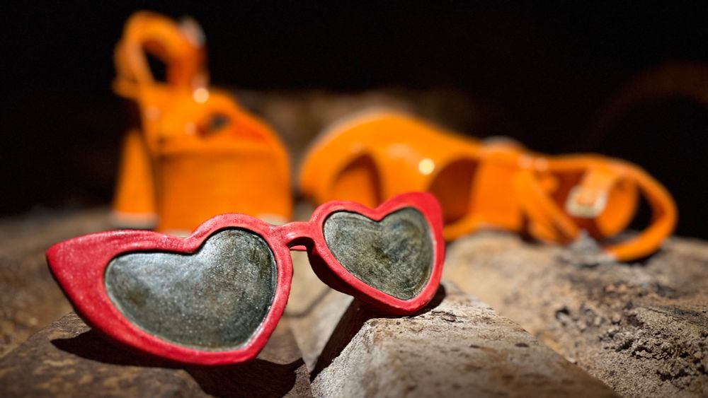 Sculpture of Red sunglasses in the foreground and orange high heeled shoes out of focus in the background 