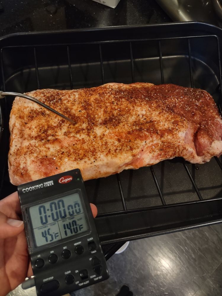 Inserting the digital probe thermometer into the thickest spot of the seasoned pork loin roast in a roasting pan with rack.