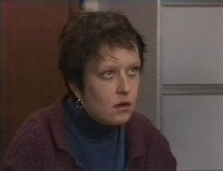 Kathy Burke, looking worried, wearing a dark blue top and dark maroon cardigan.