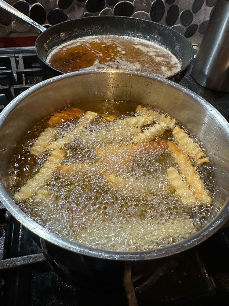 Crinkle cut Fries cooking in a pot of oil.