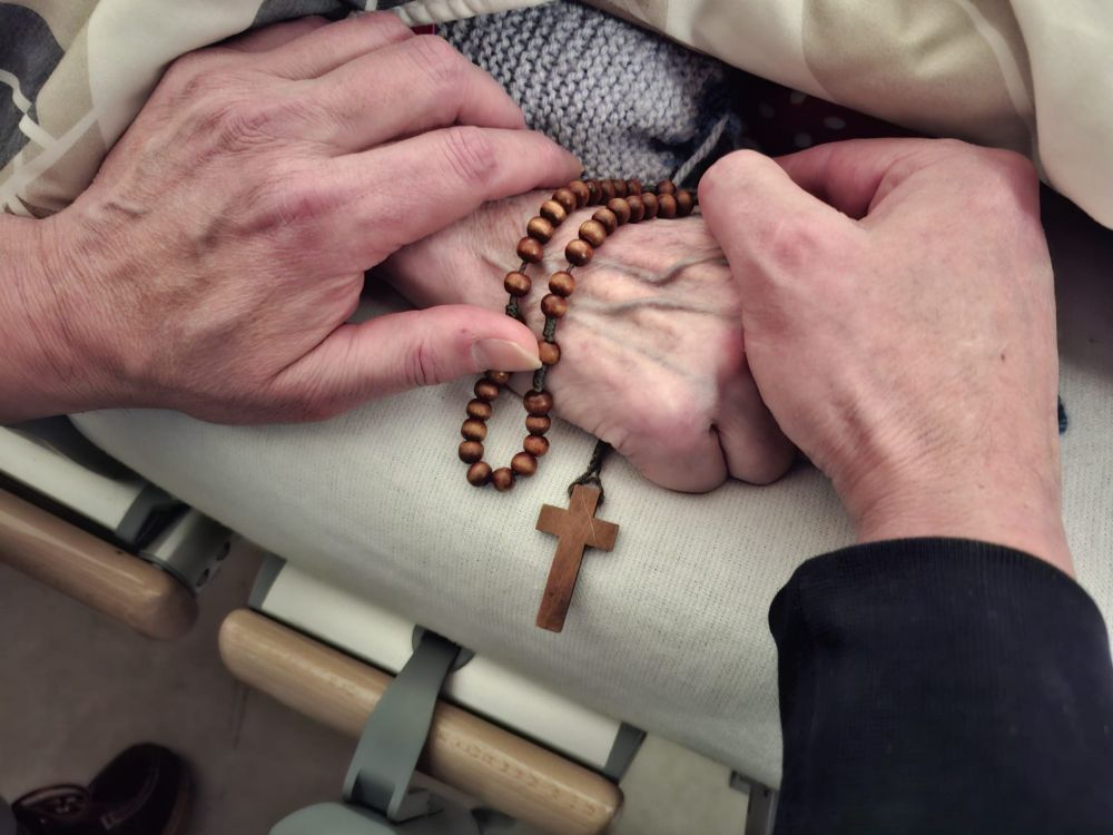 Ik houd de hand vast van mijn stervende moeder. Mama heeft de rozenkrans in haar hand.