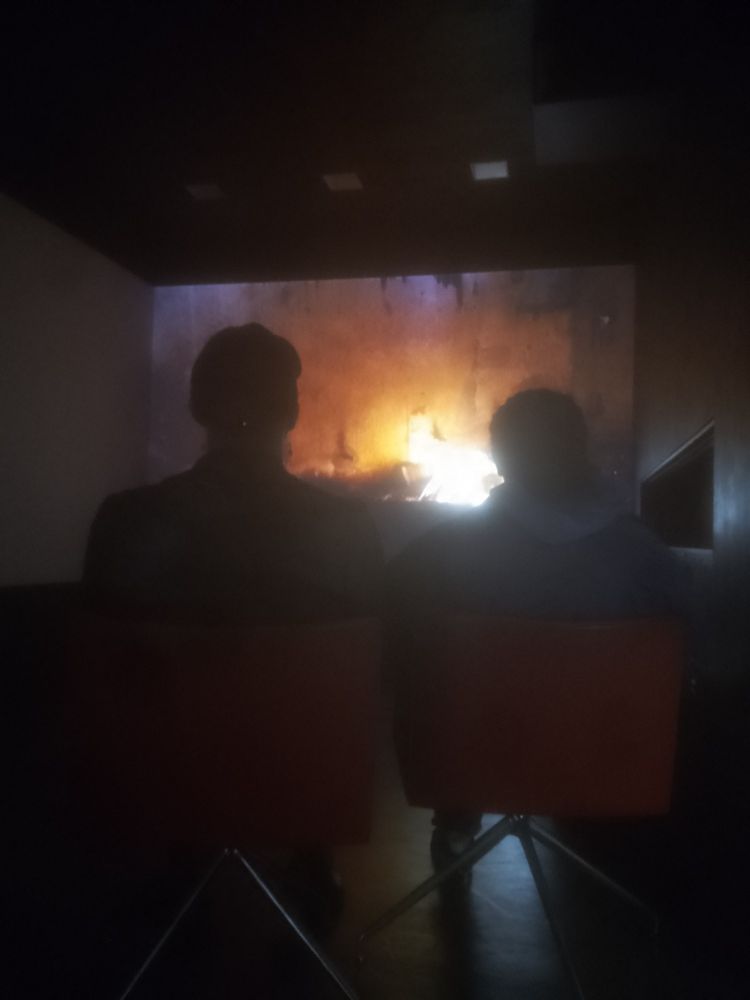 Deux jeunes hommes assis devant un film avec du feu, dans un musée