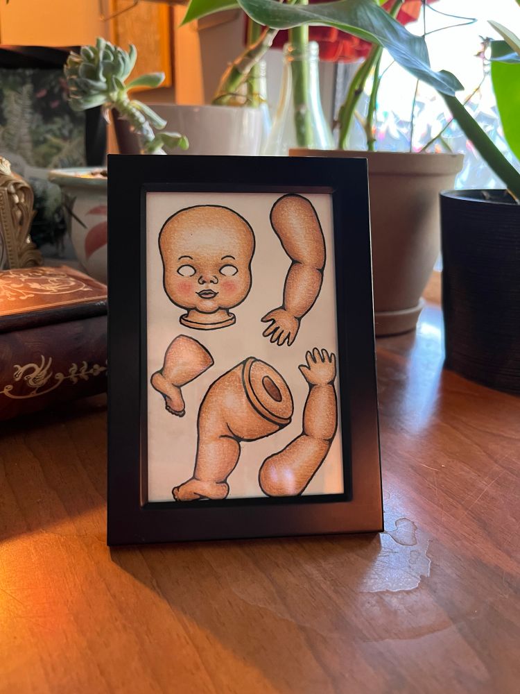 a colored pencil drawing of baby doll parts in a black frame 