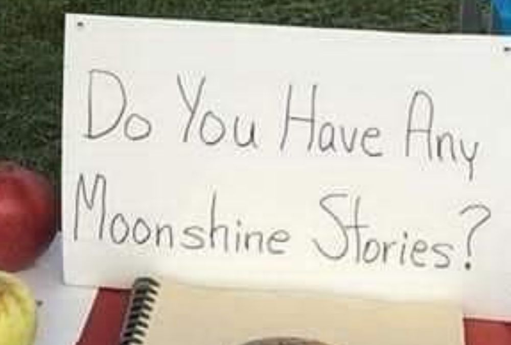 crop from one of the above images of tom at his apple stand with a sign that reads “Do You Have Any Moonshine Stories?”