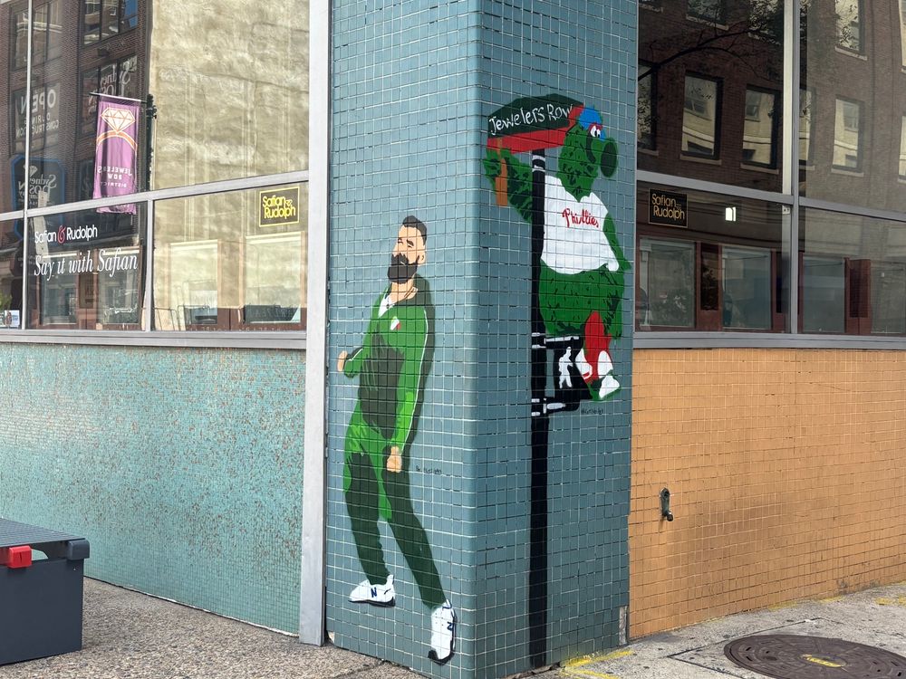 street art on a corner in jeweler’s row shows the phanatic sitting on a street post on one corner and jason kelce dancing in a green tracksuit on the other 