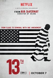 Movie poster for the documentary, 13th, by Ava DuVernay. The background is slightly beige. In the middle of the poster is the United States flag in black and white, the stripes of which match up to a black-and-white striped prison uniform worn by a Black person walking in front of the right side of the flag. There are chains around their bare feet and they’re walking off to the edge of the poster. The effect looks like the prison uniform is a part of the flag. Above the flag is written, “From slave to criminal with one amendment.” Below the flag is the title 13th in big red font.