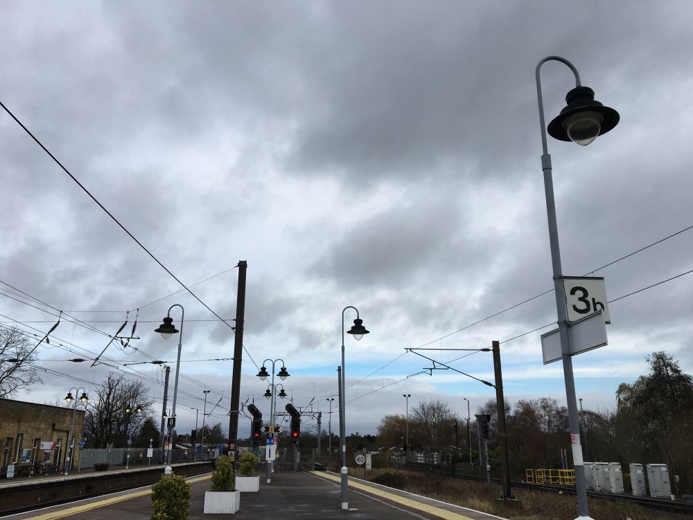 a station platform with an expanse of mostly grey sky; two long narrow patches of blue sky sandwiched between the grey
