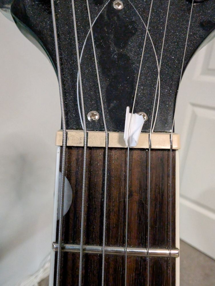 Small piece of paper slid under G string at the nut on a Gretsch to fix some minor string buzz that I can't be arsed to properly fix 