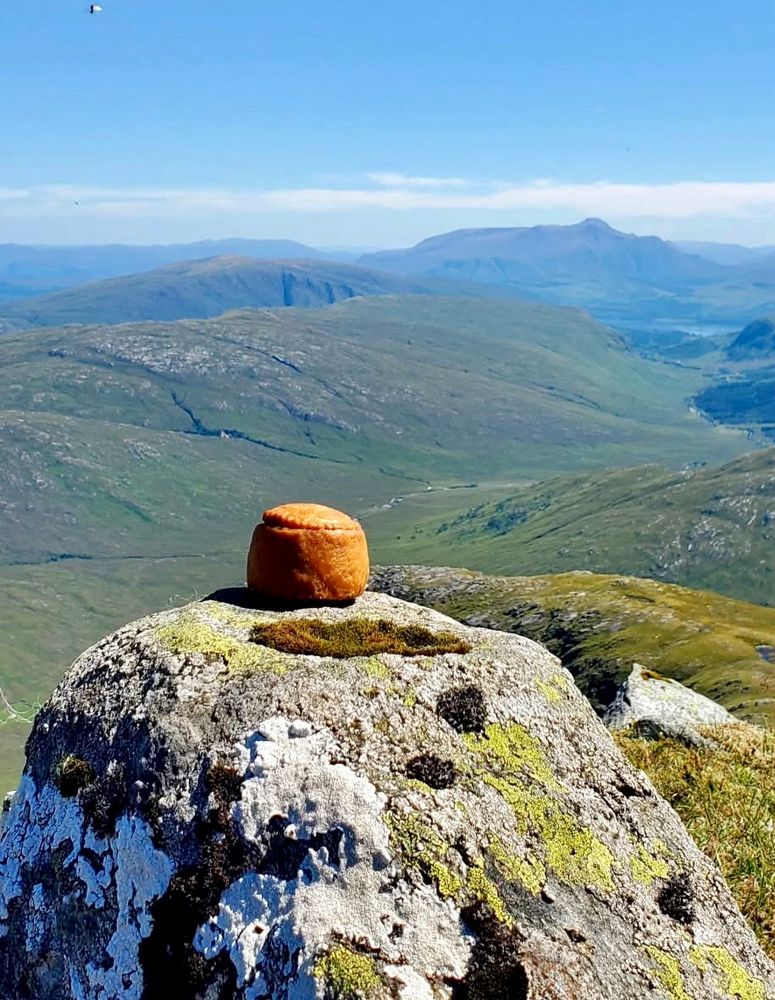 One pork pie sitting on the summit of a mountain on a sunny day in Scotland. Other mountains feature in the background, with blue skies as it was a 28c day in July. 