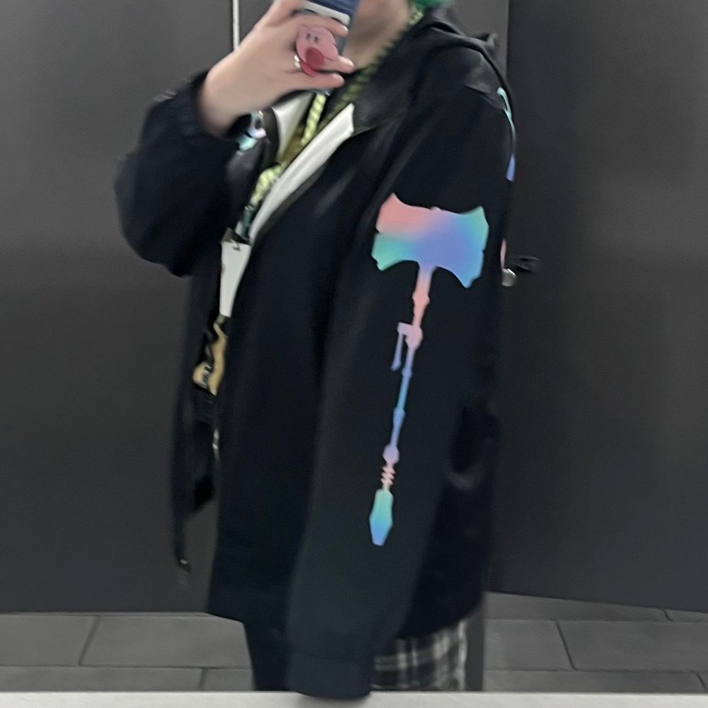side view of me wearing a black zip-up jacket with a pastel design of Jayce’s hammer on the left sleeve