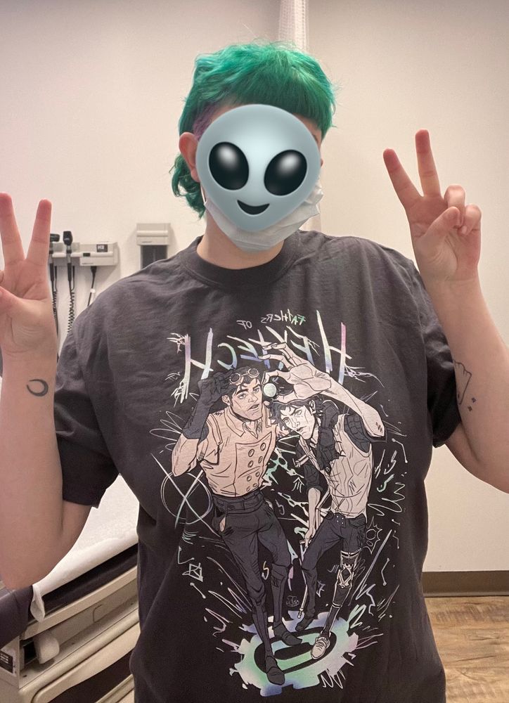 photo of me (white person with green hair) doing dual peace signs while standing in a doctors office. I’m wearing a grey shirt with art of Jayce and Viktor by @yenstlla