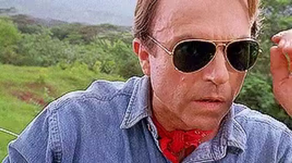 a man wearing sunglasses and a bandana is standing in front of a field .